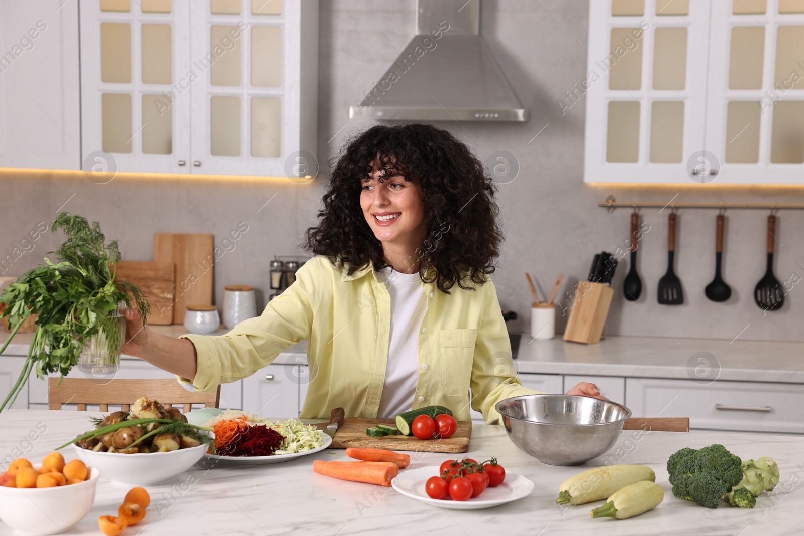 Photo of Woman cooking healthy vegetarian meal at white marble table in kitchen