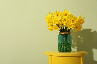 Beautiful daffodils in vase on table near light green wall, space for text