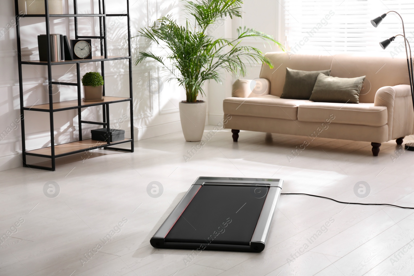 Photo of Modern walking treadmill in living room. Home gym equipment