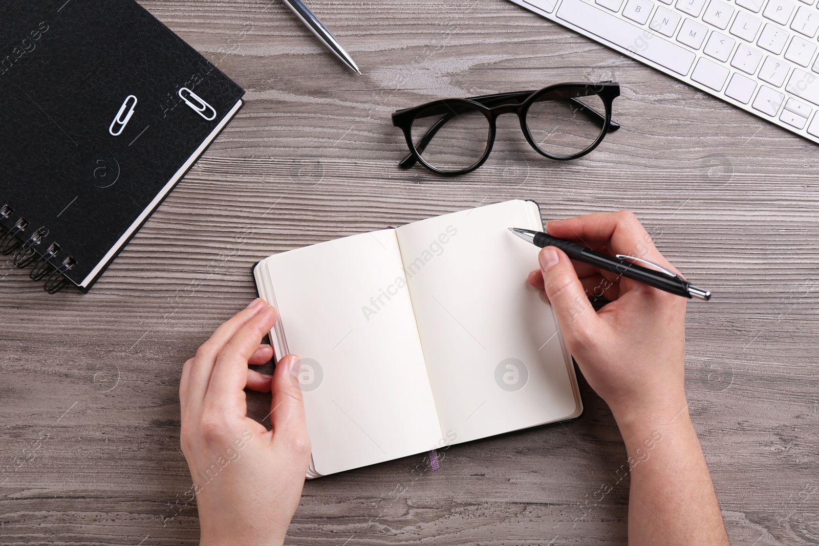 Photo of Woman writing in notebook at wooden table, top view