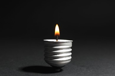 Photo of Burning candle in cap of lightbulb on black background, closeup
