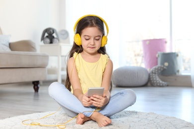 Cute child with headphones and mobile phone on floor indoors