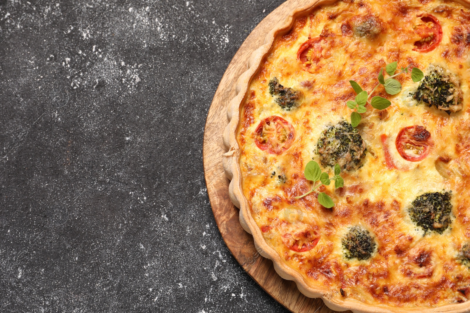 Photo of Delicious homemade vegetable quiche and oregano on black table, top view. Space for text