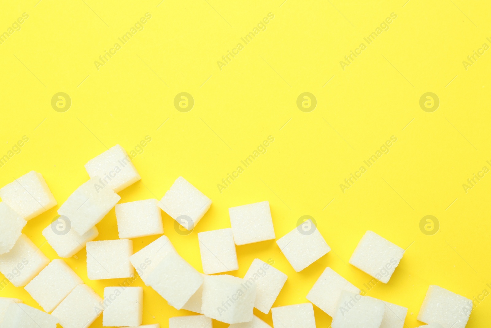 Photo of White sugar cubes on yellow background, top view. Space for text