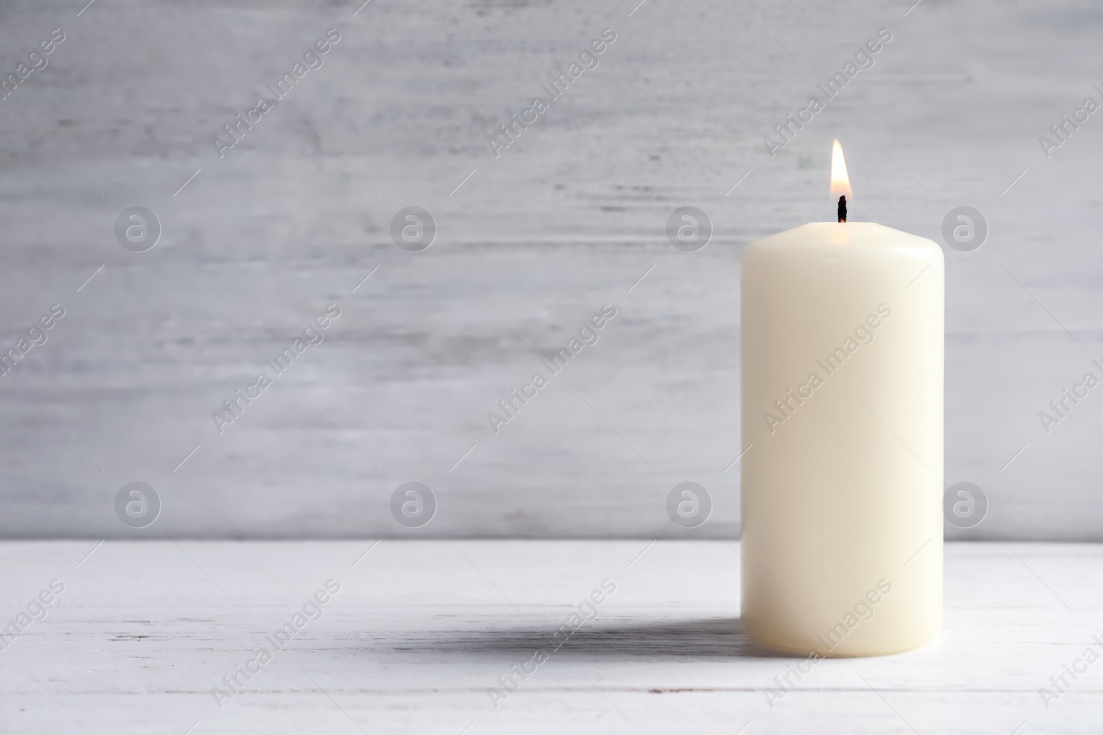 Photo of Beautiful burning wax candle on table against light background