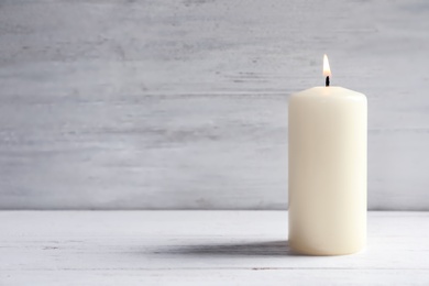 Photo of Beautiful burning wax candle on table against light background