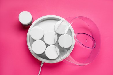 Modern yogurt maker with jars on pink background, flat lay