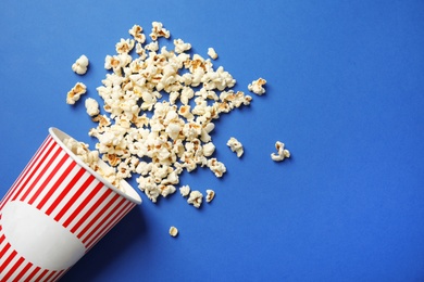 Paper cup and tasty popcorn on color background, top view with space for text. Cinema snack