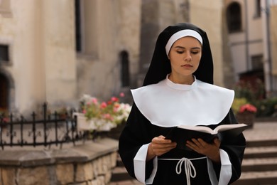 Young nun reading Bible near building outdoors, space for text