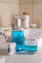 Photo of Bottle with fresh mouthwash, glass and dental floss on countertop in bathroom