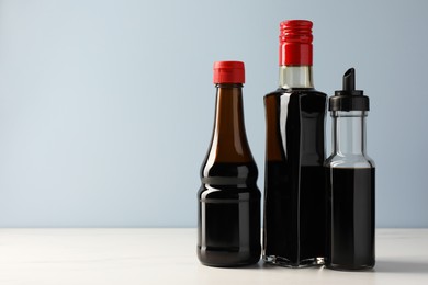 Photo of Bottles with soy sauce on white table, space for text