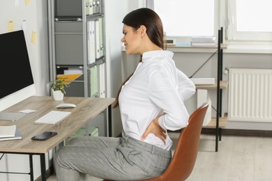 Photo of Young woman suffering from back pain while sitting in office. Symptom of scoliosis