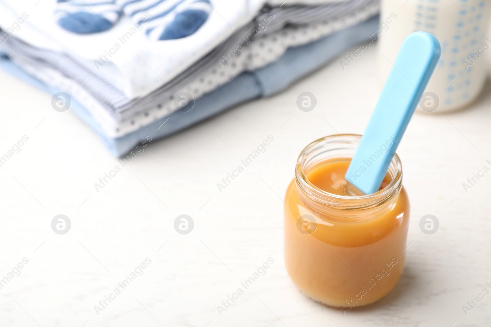 Photo of Jar with baby food and clothes on light table. Space for text