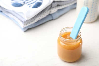 Photo of Jar with baby food and clothes on light table. Space for text