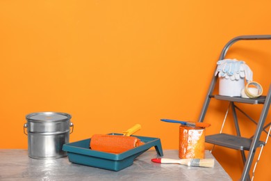 Photo of Tray with paint and roller near renovation equipment on table against orange background. Space for text