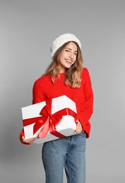 Photo of Happy young woman in Santa hat and sweater with gift box on light grey background. Christmas celebration