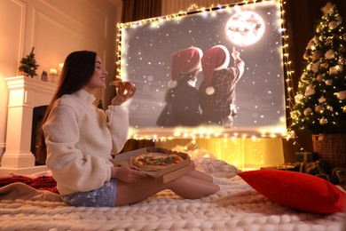 Image of Woman eating tasty and watching Christmas movie via video projector in room. Cozy winter holidays atmosphere
