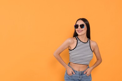 Photo of Attractive happy woman in fashionable sunglasses against orange background. Space for text