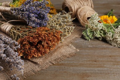 Photo of Different herbs, thread and burlap fabric on wooden table, closeup. Space for text