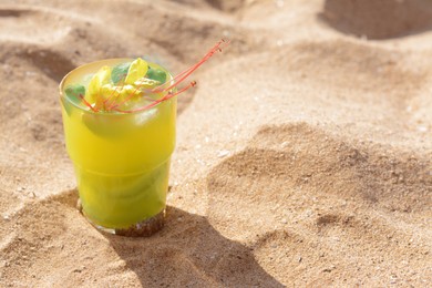 Photo of Glass of refreshing drink on sand. Space for text