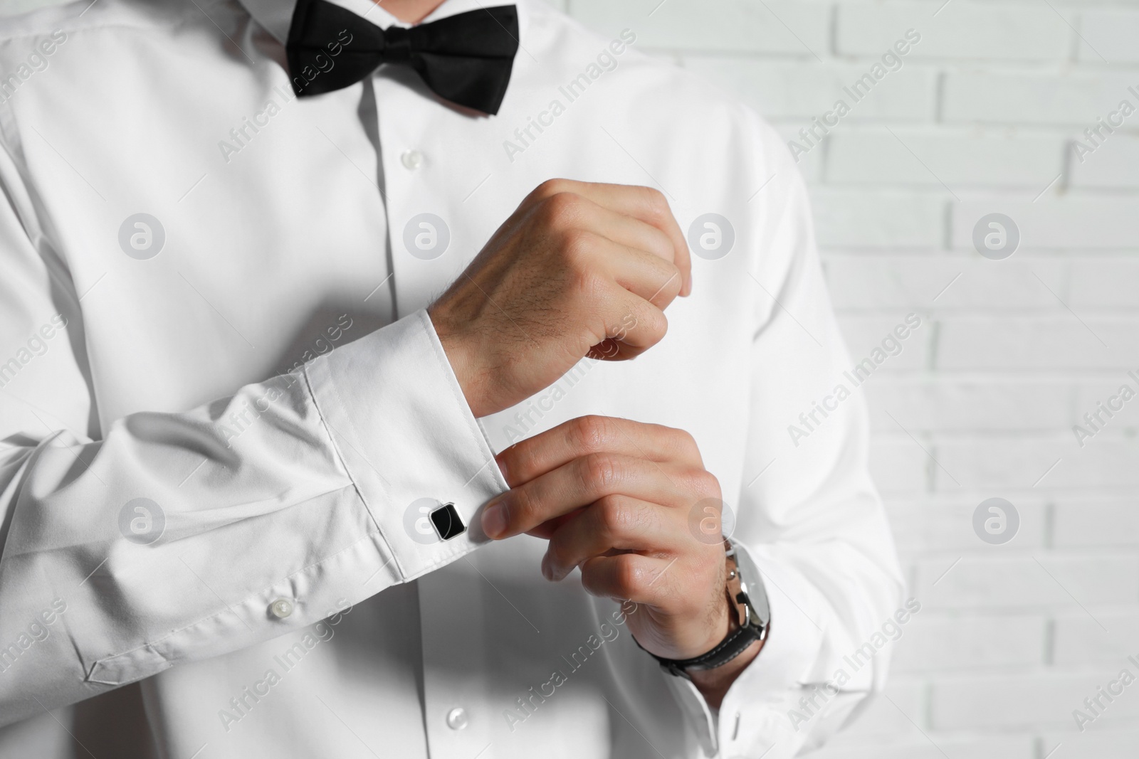 Photo of Stylish man putting on cufflink near white brick wall, closeup