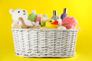 Photo of Wicker basket with baby cosmetic products and accessories on yellow background