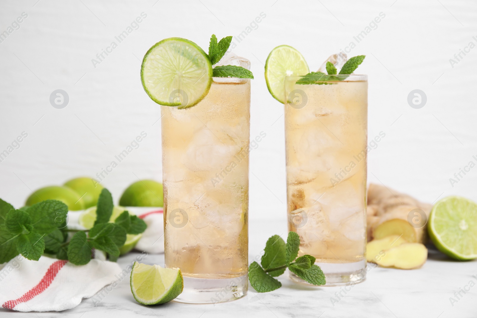 Photo of Glasses of tasty ginger ale with ice cubes and ingredients on white marble table