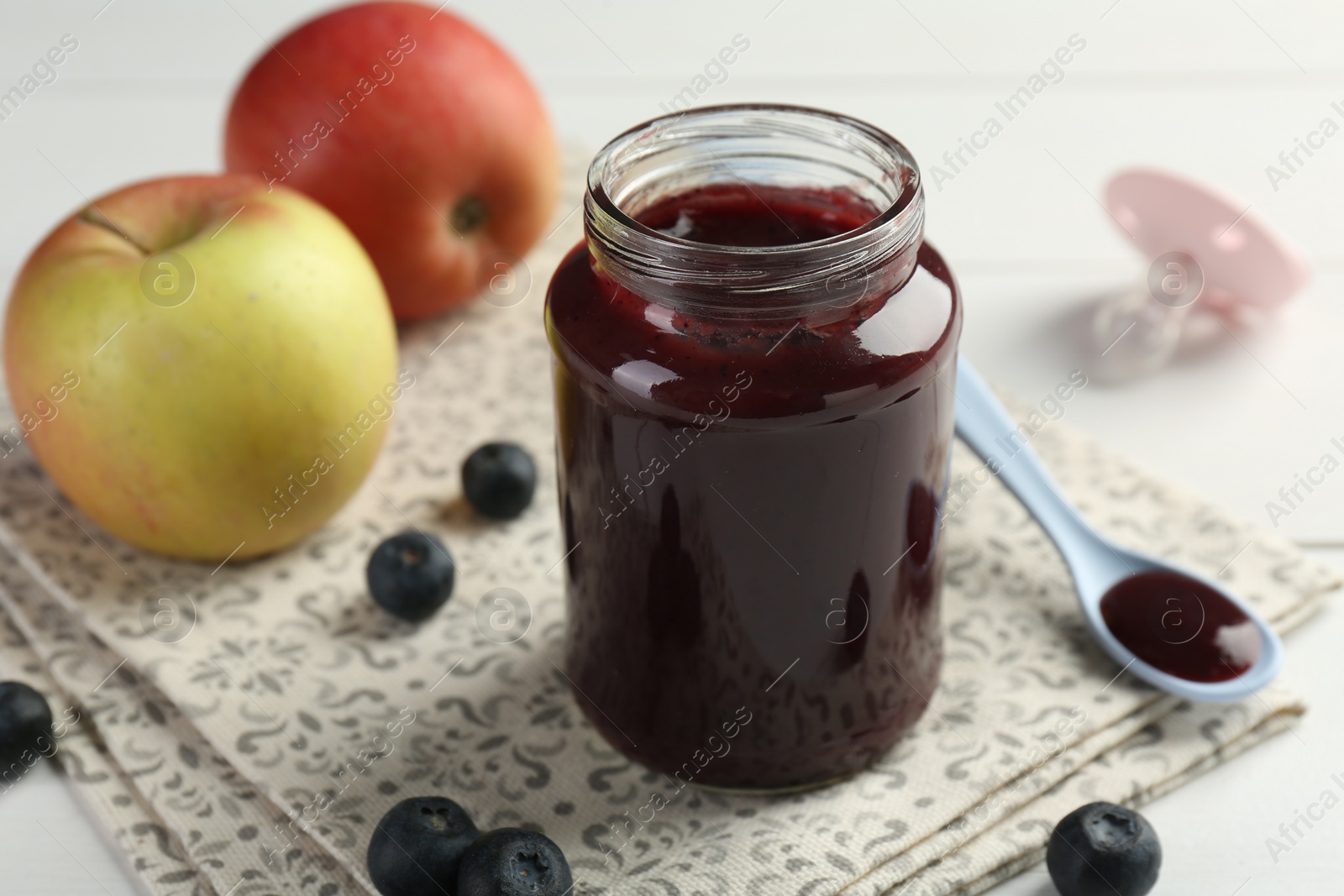 Photo of Tasty baby food in jar, blueberries and apples on white table, closeup