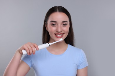 Happy young woman holding electric toothbrush on light grey background