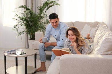 Photo of Man with cup and reading woman on sofa in living room