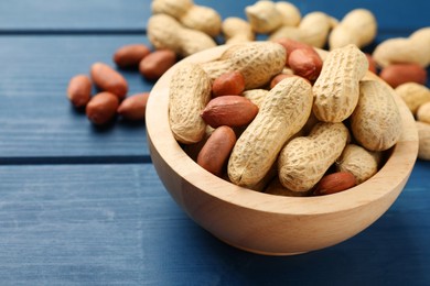 Photo of Fresh unpeeled peanuts in bowl on blue wooden table, closeup. Space for text