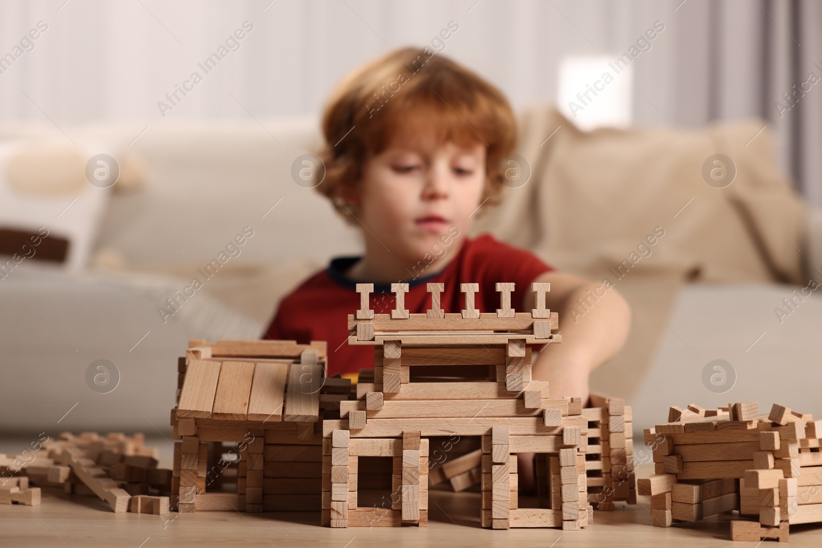 Photo of Cute little boy playing with wooden construction set at table in room, selective focus. Child's toy