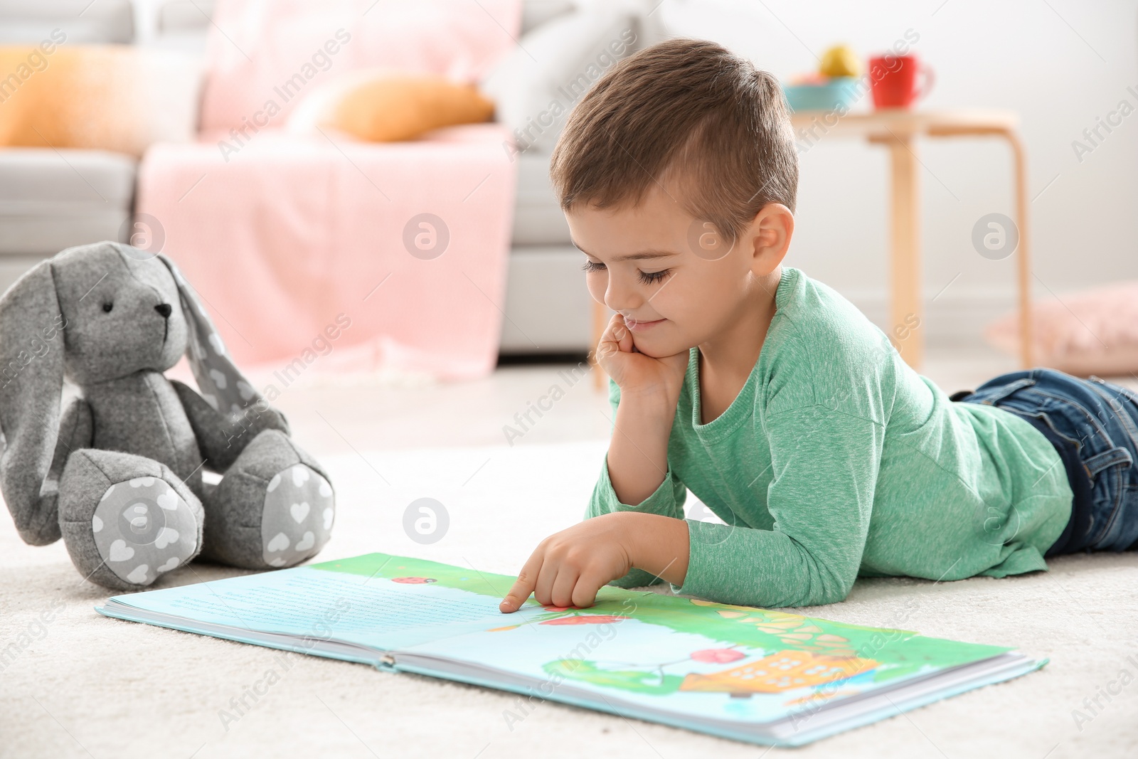 Photo of Little boy with toy reading book on floor at home