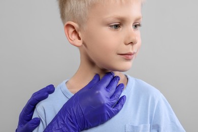 Endocrinologist examining boy's thyroid gland on light grey background, closeup