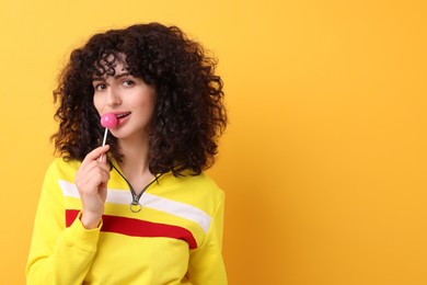 Beautiful woman with lollipop on yellow background, space for text