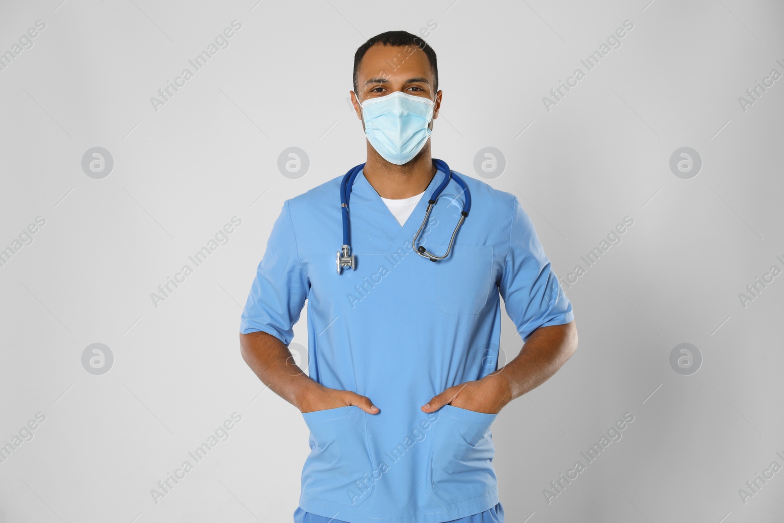 Photo of Doctor or medical assistant (male nurse) with protective mask and stethoscope on light grey background