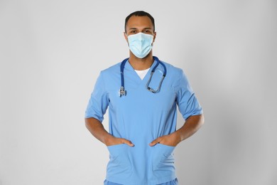 Photo of Doctor or medical assistant (male nurse) with protective mask and stethoscope on light grey background