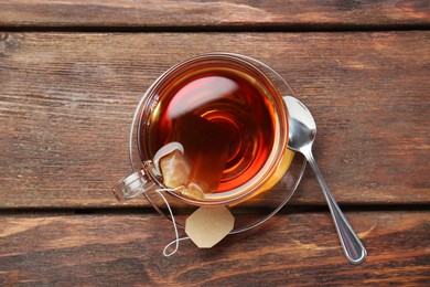 Photo of Brewing aromatic tea. Cup with teabag and spoon on wooden table, top view