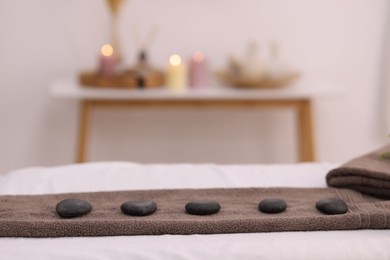 Photo of Towel with arranged spa stones on massage table in recreational center, closeup