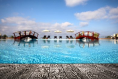 Image of Empty wooden surface near outdoor swimming pool with clear water. Space for design