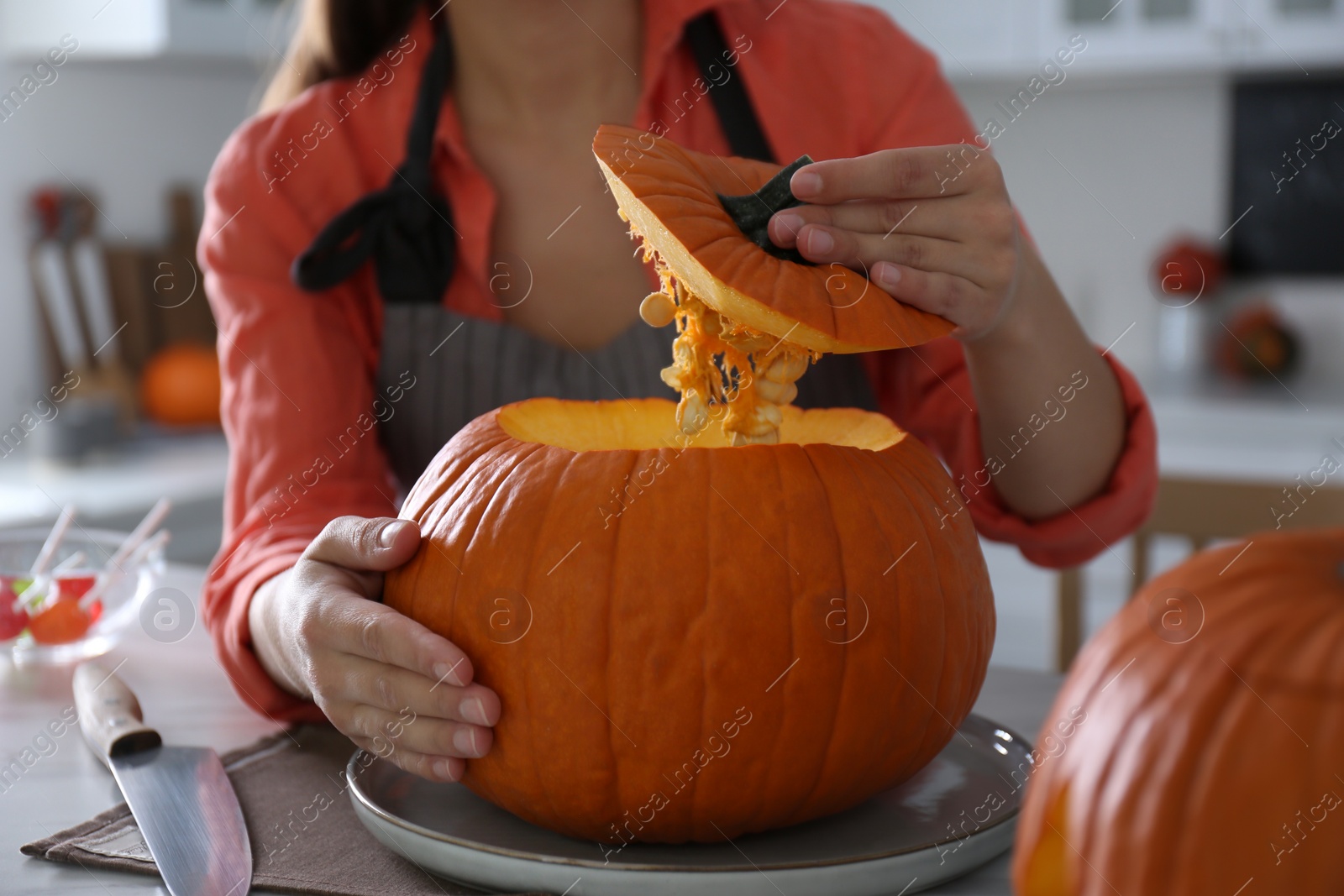 Photo of Woman making pumpkin jack o'lantern at table in kitchen, closeup. Halloween celebration