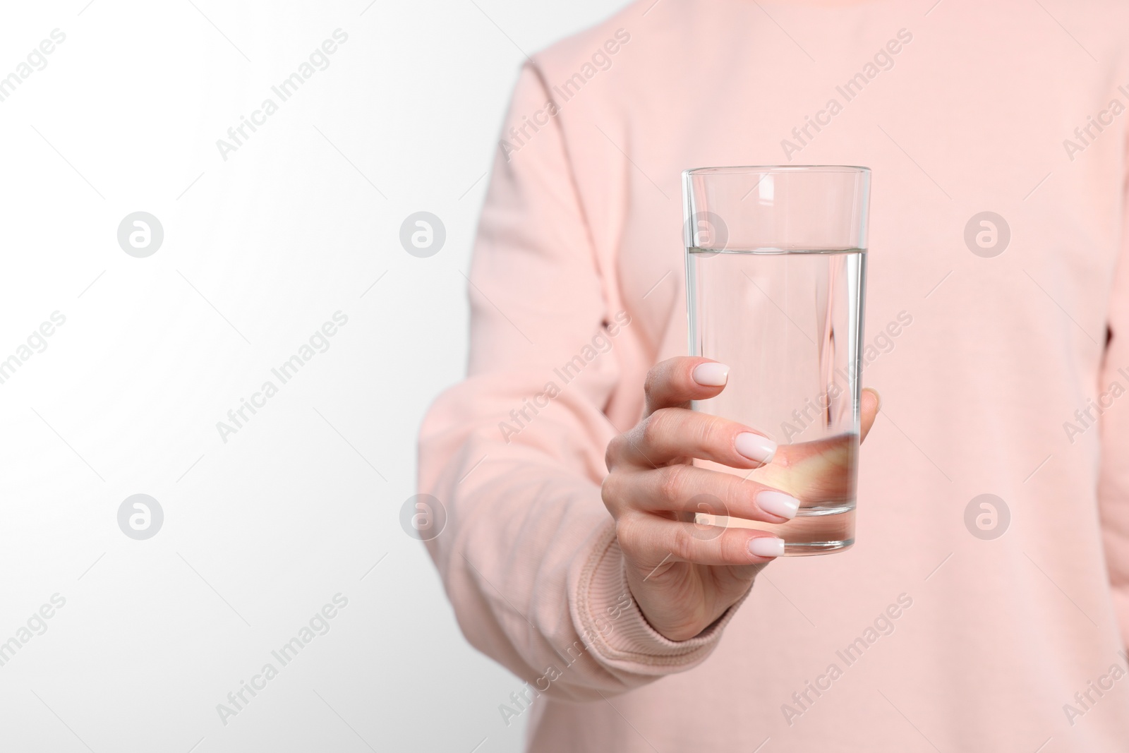 Photo of Healthy habit. Closeup of woman holding glass with fresh water on light grey background, space for text