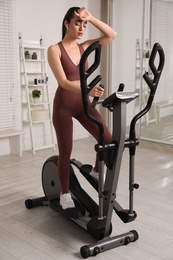 Young woman feeling tired of training on 	
elliptical machine at home