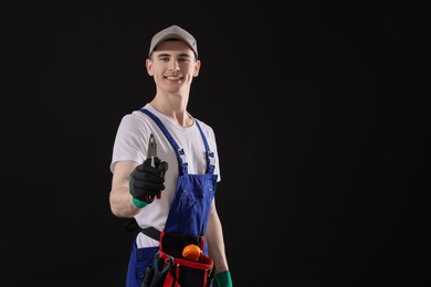 Photo of Young man holding pliers on black background, space for text