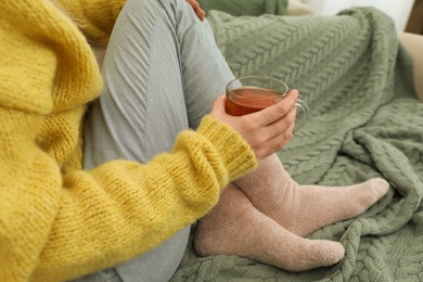 Photo of Woman with cup of tea sitting on sofa with green plaid, closeup