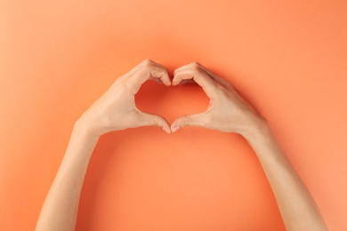 Photo of Woman making heart with her hands on color background, top view