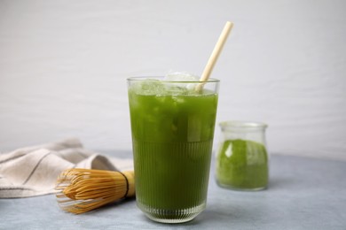 Glass of delicious iced green matcha tea and bamboo whisk on light grey table