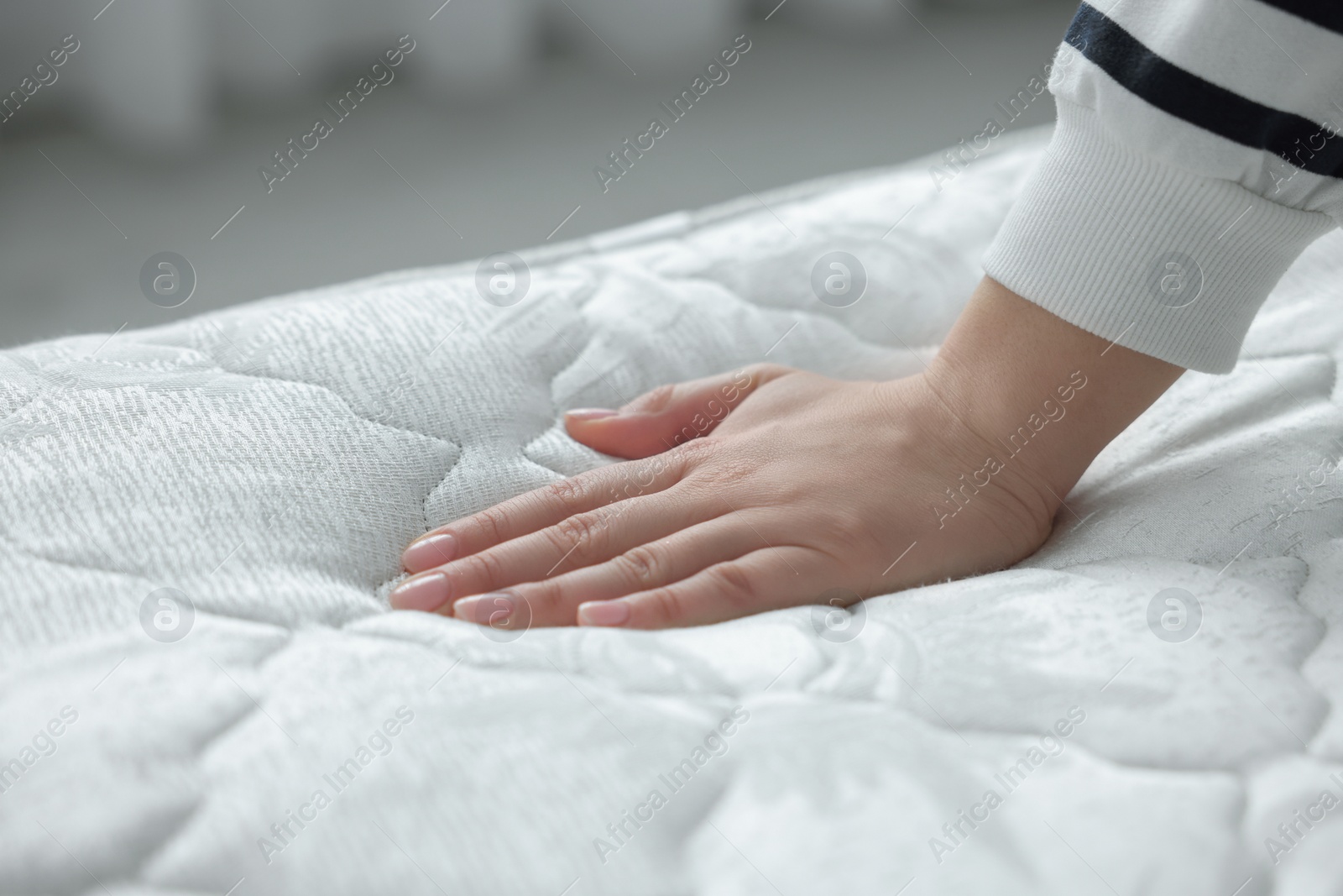 Photo of Woman touching soft white mattress indoors, closeup