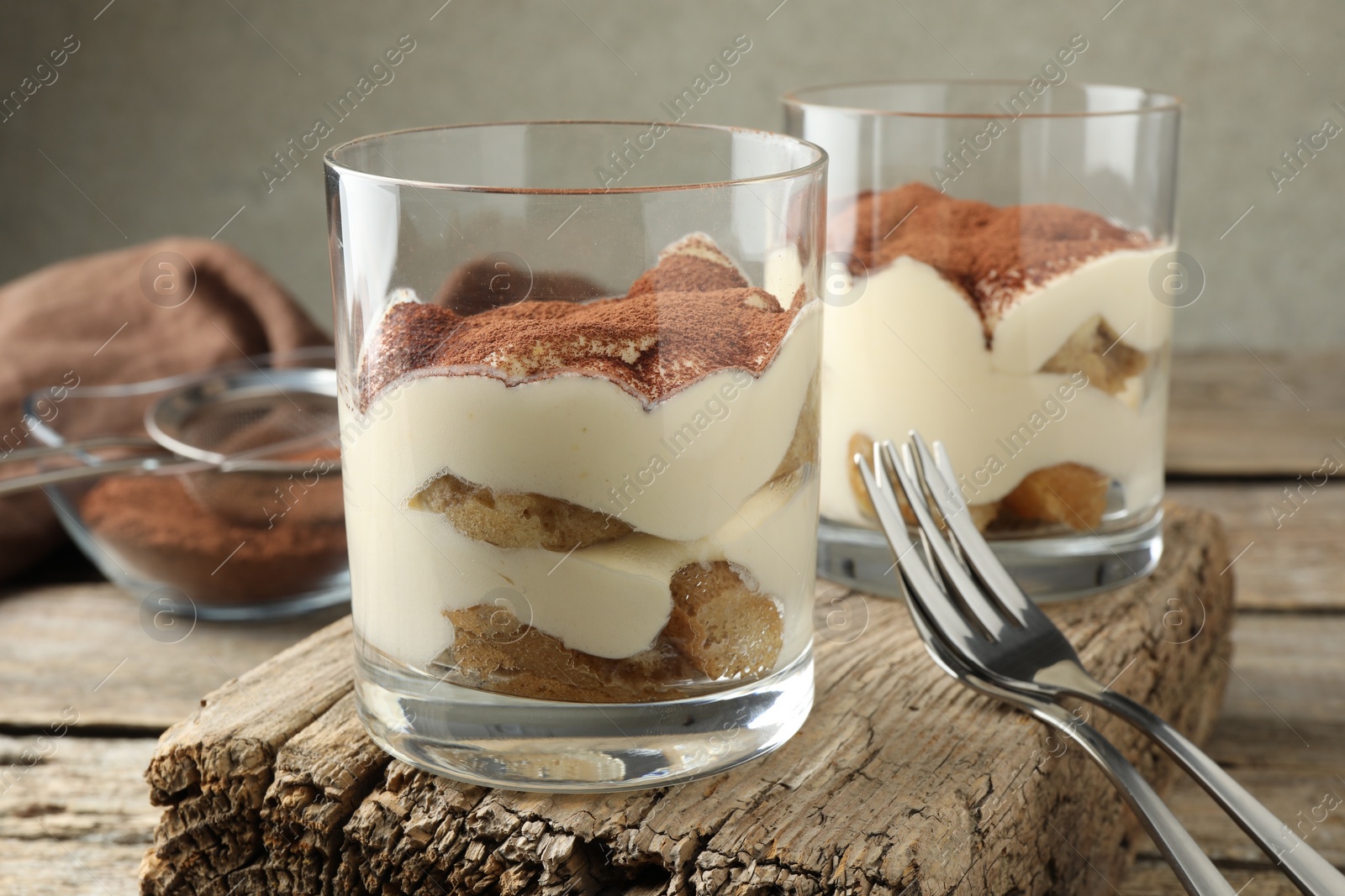 Photo of Delicious tiramisu in glasses and forks on wooden table, closeup