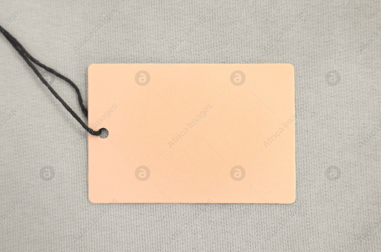 Photo of Cardboard tag on beige garment, top view. Space for text